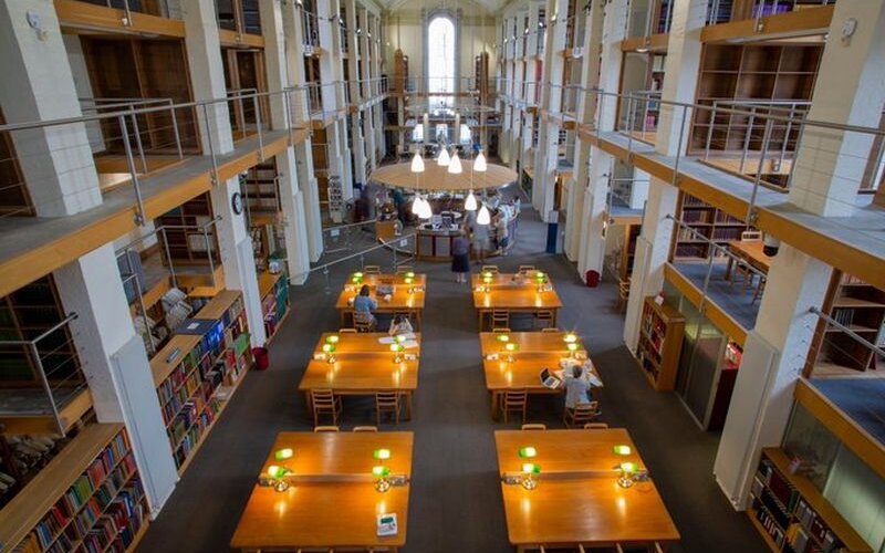 A view looking down on the Library's Reading Room with wooden desks in the centre and different levels of shelving to either side
