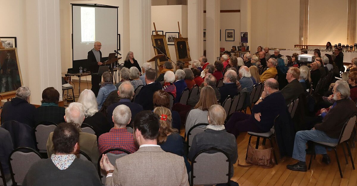 Audience listening to a presentation by two people in the Gregynog Gallery