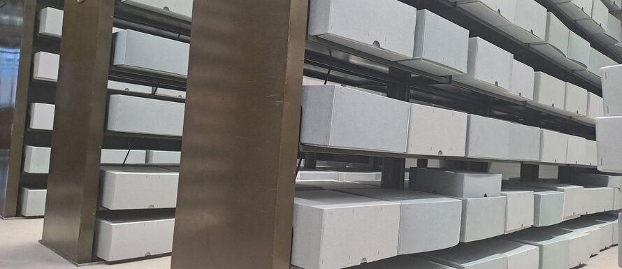 Photo showing the shelving and boxes containing BBC scripts. The boxes are grey and the shelving is brown.