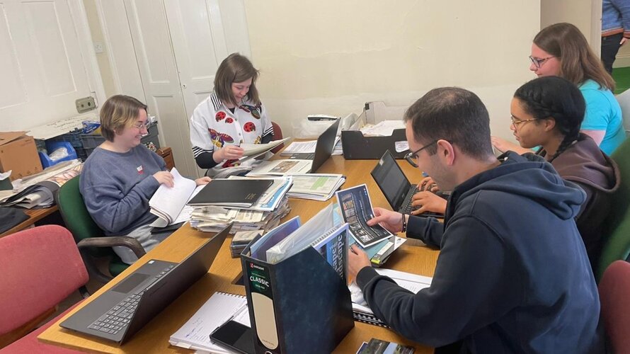 An image of students working around a desk holding archival boxes and papers