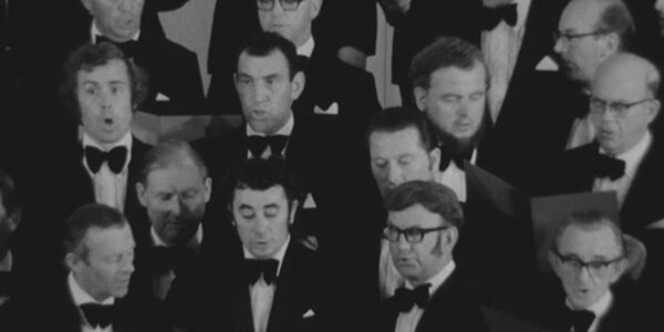 A black and white image showing members of a male voice choir singing.