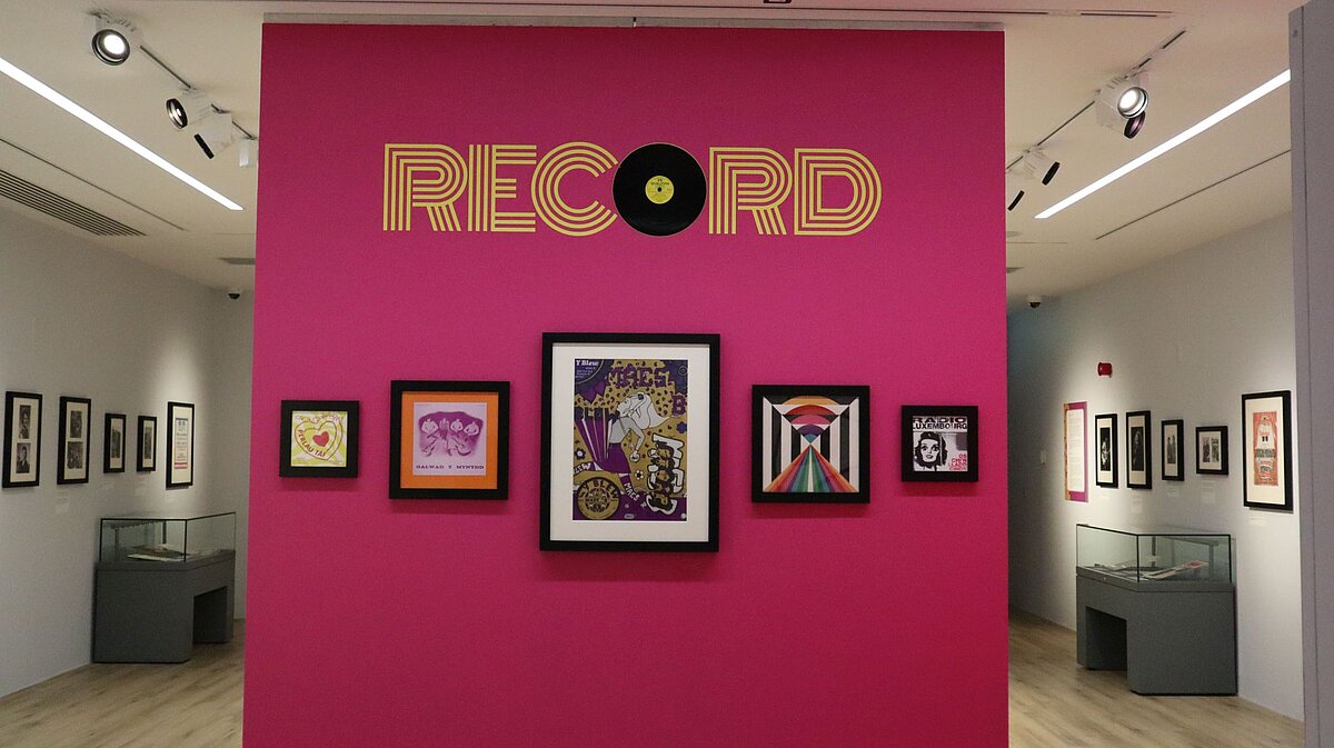 Image of the pink exhibition entrance wall including mounted photographs and the word 'Record'