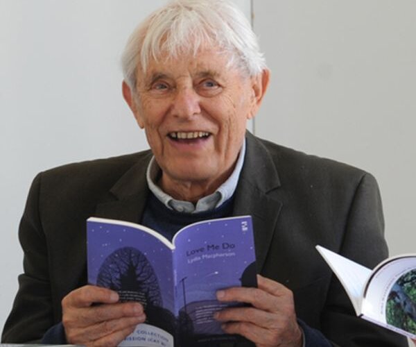 A photograph of the Welsh poet Dannie Abse smiling and holding a book open
