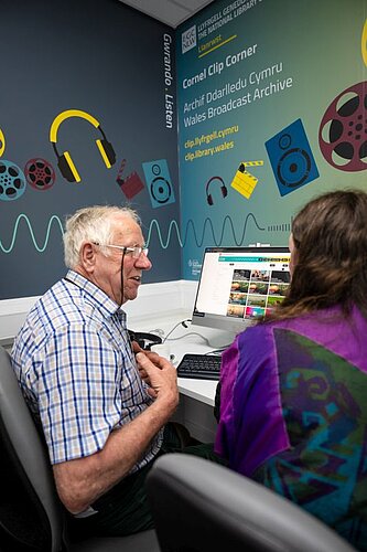 Two people looking at the Clip Cymru website on a PC