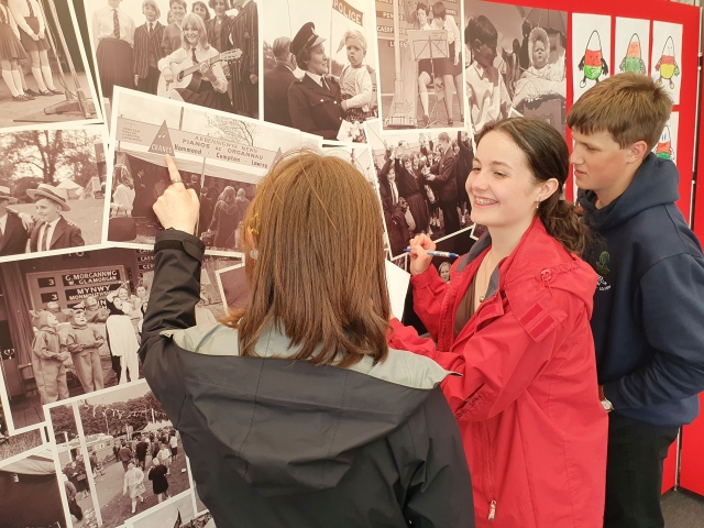 Three young people looking at photographs on a wall in the National Library tent in the Eisteddfod h