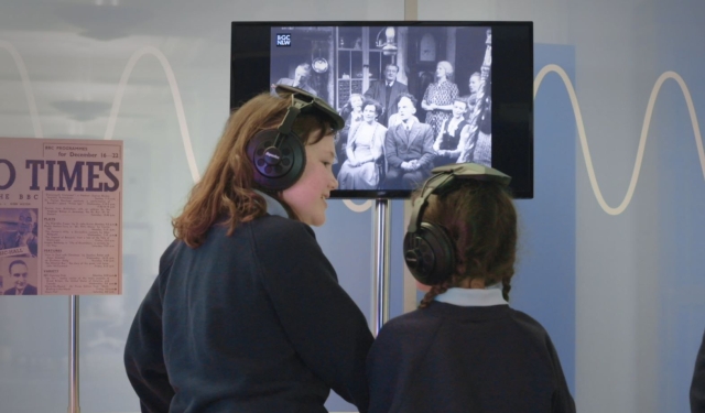Two children using headphones to watch a clip on a screen h