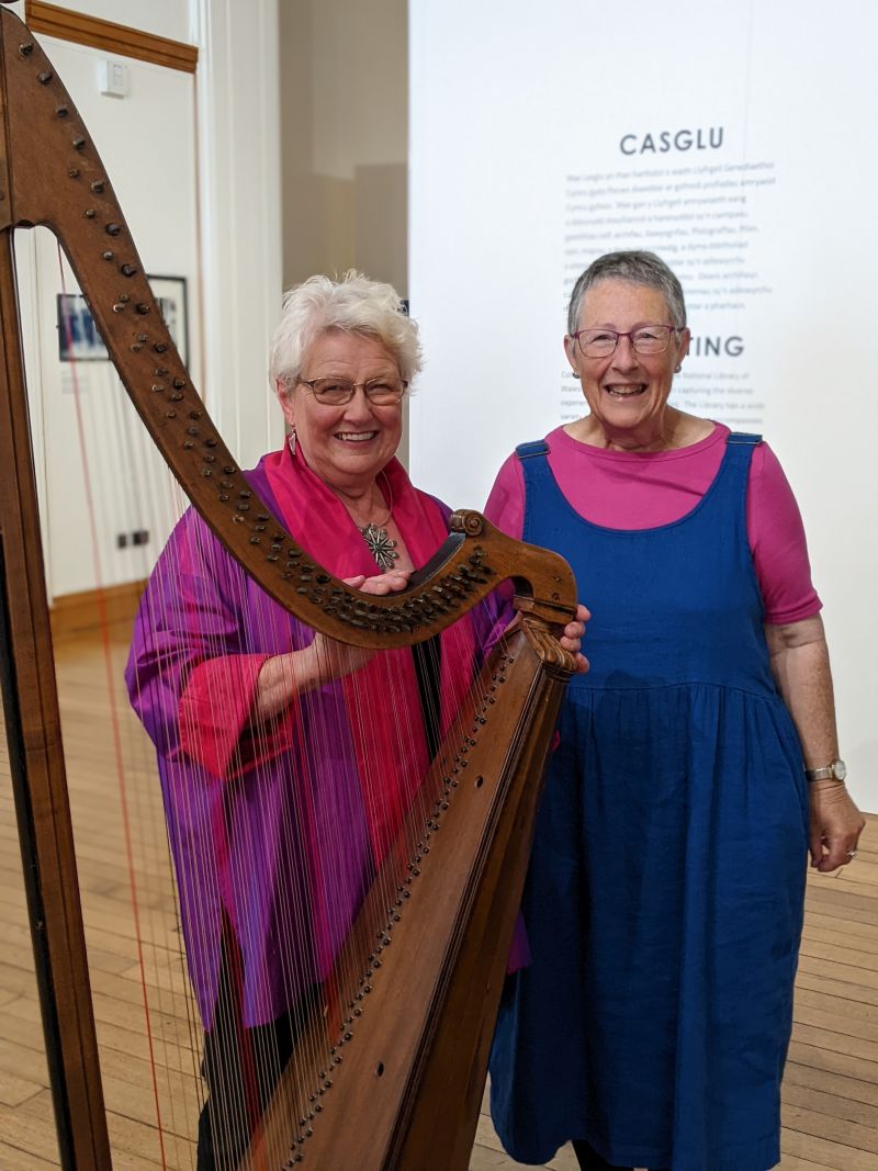 Elinor Bennett and Eluned Evans standing with a harp at the Library