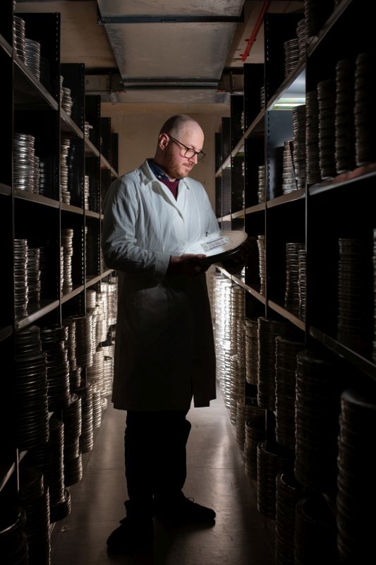 Person in white coat looking at the audio visual collections on the shelves