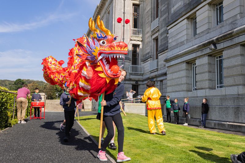Children with a large Chinese dragon outside the front of the Library building
