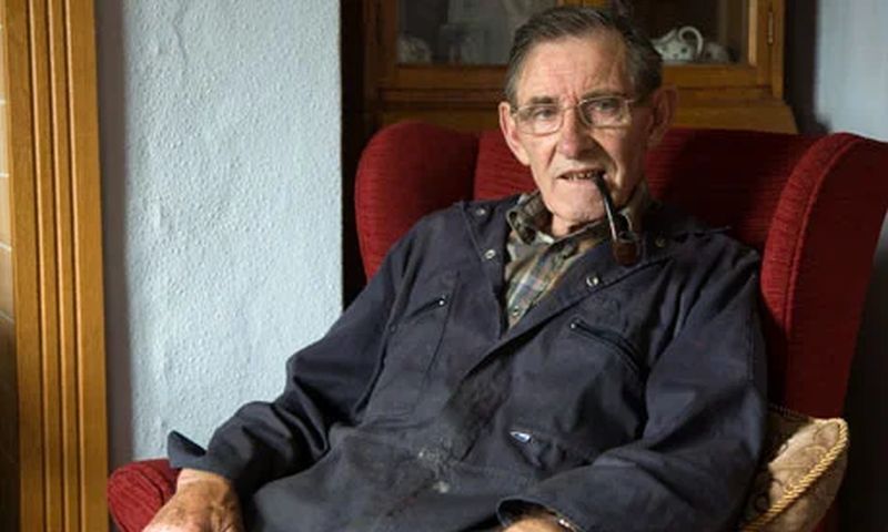 A photograph of Dic Jones wearing a blue overall and leaning back in a red chair