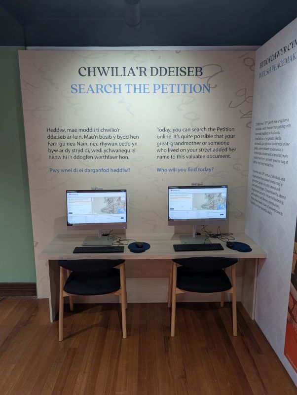 A desk with two PCs below a sign reading 'Search the Petition'