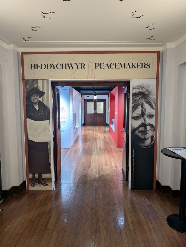 The entrance to the 'Peacemakers' exhibition, showing a doorway with a sign above reading 'Heddychwyr/Peacemakers'